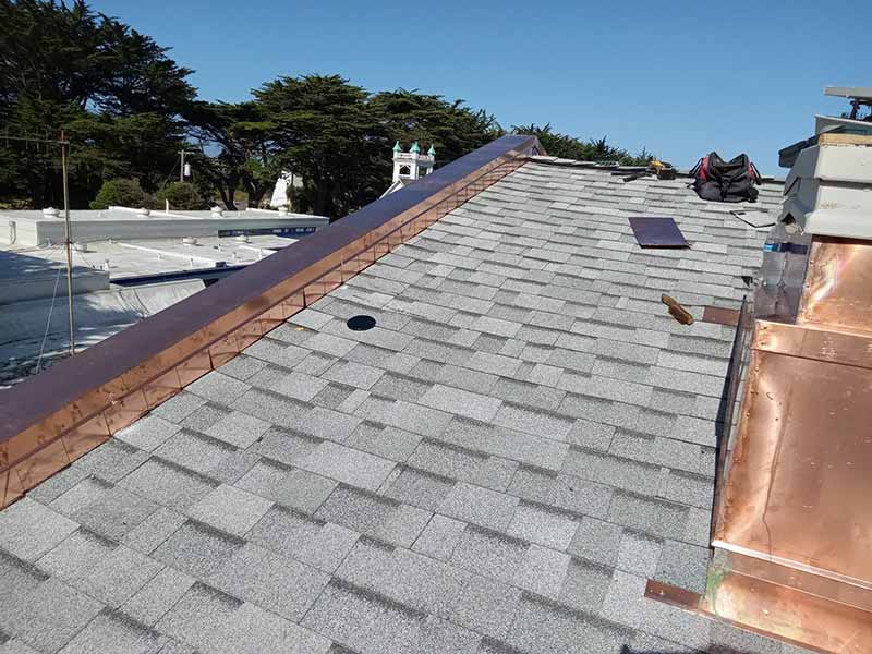 Close up of a sloped residential roof with bronze flashing and gray shingles newly installed by Henris Roofing Company